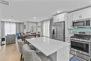 A modern kitchen with white cabinets, stainless steel appliances, a central island with seating, and a dining area with a table and chairs.