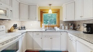 Eine Küche mit weißen Schränken, einem Fenster, einer eingebauten Mikrowelle, einem Toaster und einer Kaffeemaschine.
