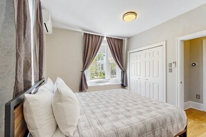 A bedroom with a bed, curtains, an air conditioning unit, a window, and a door.