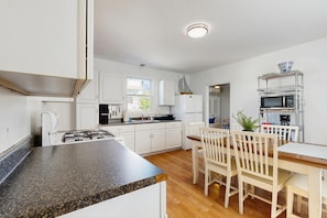 A modern kitchen with white cabinets, a granite countertop, a dining area with wooden chairs, and a built-in microwave shelf.