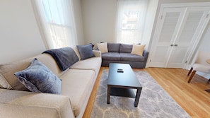 A living room with a beige sofa, a dark-colored coffee table, and a gray rug.