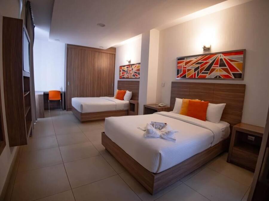 Habitación de hotel con dos camas, cabecera de madera, mesita de noche, lámpara de pared y un cuadro.