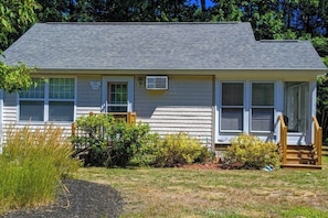 A single-story house with a gray roof, white siding, and a front porch with a wooden railing.