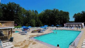 Une piscine entourée d’arbres, avec des chaises longues et des parasols.