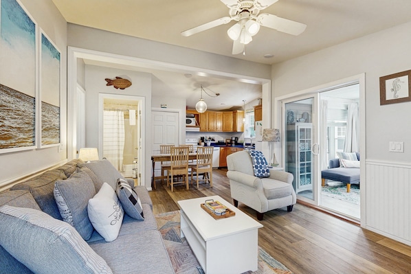 A living room with a sofa, armchair, and coffee table, a dining area with chairs, and a kitchen in the background.
