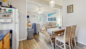 Une cuisine équipée d’un réfrigérateur, d’une table à manger avec des chaises, d’un ventilateur de plafond et donnant sur le salon.