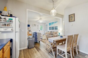 Eine Küche mit Kühlschrank, einem Esstisch mit Stühlen, einem Deckenventilator und Blick auf das Wohnzimmer.