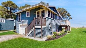 A two-story house with a front deck, a garage, and a well-maintained lawn. - Ocean and Sunset Views: semi private sandy beach, close to dining & Route 1 (Biddeford)