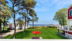 A deck with a red umbrella, a grassy lawn, and a view of the ocean. - Ocean and Sunset Views: semi private sandy beach, close to dining & Route 1 (Biddeford)