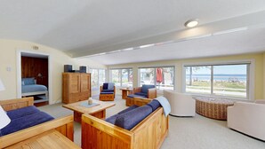 A spacious room with a bed, wooden furniture, a small table, and large windows offering a view of the beach. - Ocean and Sunset Views: semi private sandy beach, close to dining & Route 1 (Biddeford)