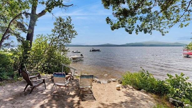 A lakeside view with a sandy beach, a wooden bench, and a boat dock.