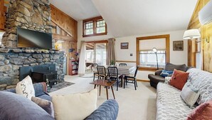 A cozy living room with a stone fireplace, a dining area, and a sofa.