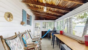 A covered porch with wooden chairs, a table, and a view of the outdoors.