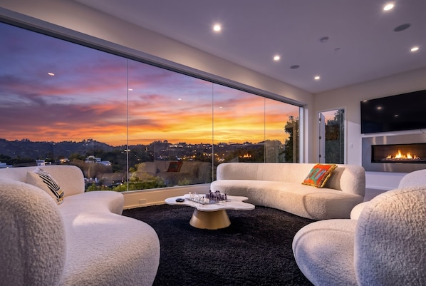 Ein modernes Wohnzimmer mit einem großen Fenster, einem Kamin und Blick auf einen Sonnenuntergang.