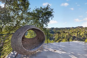 Ein Korbstuhl auf einem Balkon mit Metallgeländer, mit Blick auf eine grüne Landschaft.