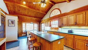 Una cocina con armarios de madera, una isla grande con taburetes y un ventilador de techo.