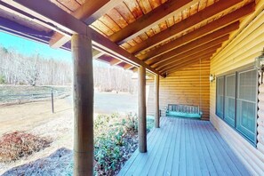 Eine überdachte Veranda mit Holzbalken, einer Bank und Blick auf eine Straße und Bäume.