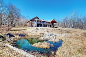 Eine Lodge mit einem großen Teich, umgeben von Bäumen und blauem Himmel.