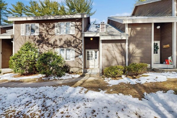 A two-story residential building with a front porch, a small front yard with snow, and a mailbox. - Four-level townhome with gas fireplace and seasonal pool in North Conway (Conway)