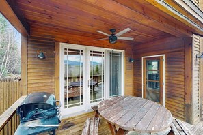 Une terrasse en bois avec une table et des chaises, un ventilateur de plafond et un barbecue.