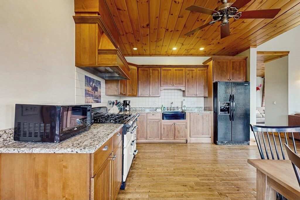 Una cocina con armarios de madera, microondas, refrigerador y ventilador de techo.