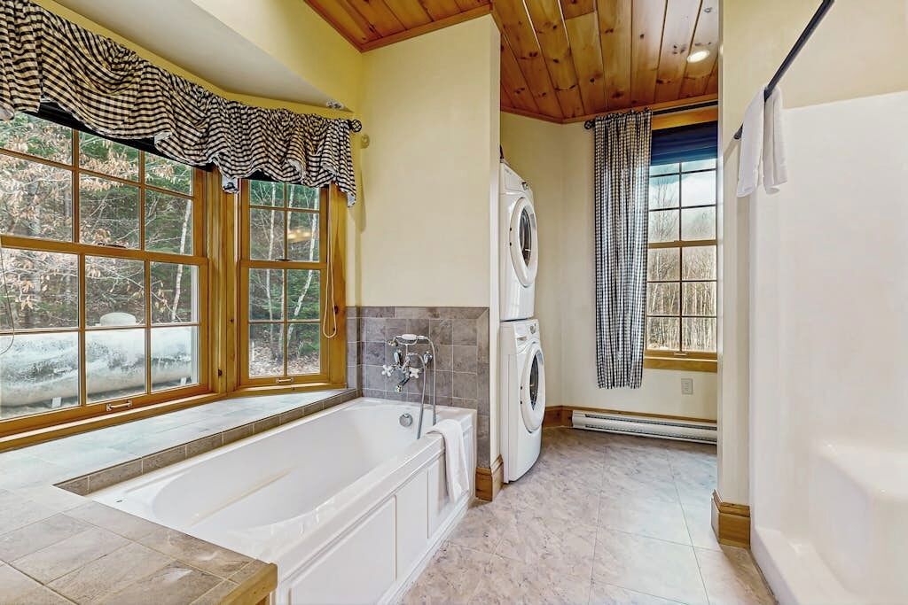 Casa de banho com banheira, máquina de lavar roupa e janela com vista para árvores.