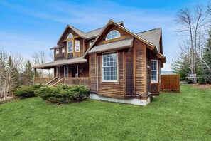 A two-story wooden house with a porch, a covered deck, and a well-maintained lawn.