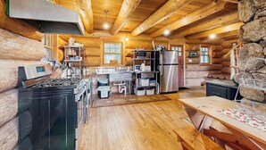 L’intérieur d’une cabane en rondins comprend une cuisine, un coin repas et un mur en pierre.