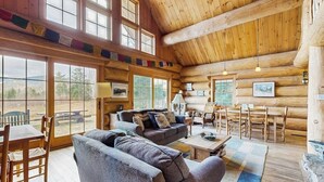 L’intérieur d’une cabane en rondins comprend un coin repas, des canapés et une grande fenêtre donnant sur l’extérieur.