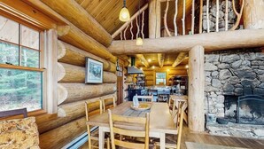 L’intérieur d’une cabane en rondins comprend un coin repas, une cuisine et une cheminée en pierre.