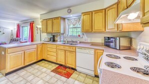 Keittiössä on puukehikoiset kaapit, astianpesukone, liesi, mikroaaltouuni ja ikkuna, jossa on verhot.