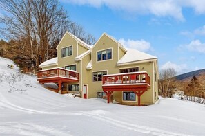 A two-story building with a balcony on the second floor, surrounded by snow. - New Slopeside Home at Black Mountain w/ Mountain Views, AC, Deck, Grill & WiFi (Jackson)