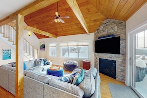 A living room with a stone fireplace, a large flat-screen TV, a wooden ceiling, and a staircase. - New Slopeside Home at Black Mountain w/ Mountain Views, AC, Deck, Grill & WiFi (Jackson)