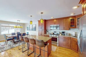 A modern kitchen with wooden cabinets, a central island with bar stools, stainless steel appliances, and pendant lighting. - New Slopeside Home at Black Mountain w/ Mountain Views, AC, Deck, Grill & WiFi (Jackson)