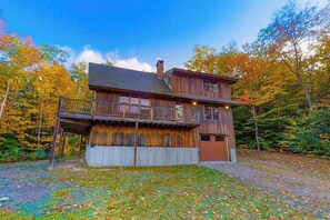 A two-story wooden cabin with a balcony, surrounded by autumn foliage.