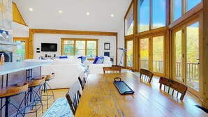 Une pièce spacieuse avec une table à manger en bois, des tabourets de bar, un canapé et de grandes fenêtres.