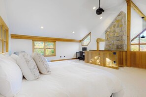 A bedroom with a large bed, wooden beams, a stone fireplace, and a desk area.