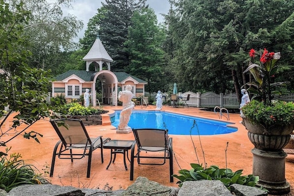 A pool area with lounge chairs, a gazebo, and statues.