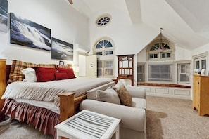 A bedroom with a large bed, a sofa, a small table, and a window with shutters.
