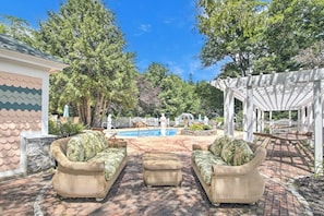 A patio with wicker furniture, a pool, and a pergola.