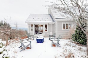 Ein Haus mit einer überdachten Außenbereich-Sitzgruppe, einem mit Schnee bedeckten Deck und Blick auf die umliegende Landschaft.