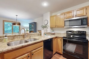 A kitchen with granite countertops, wooden cabinets, a stainless steel sink, a dishwasher, a microwave, and an oven. - Homey Mountain Retreat: close to skiing and all season outdoor adventures (Lincoln)
