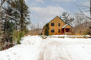 A two-story wooden house with a stone foundation, surrounded by snow-covered ground and trees. - Cozy, Dog-Friendly Home with High-Speed WiFi & Deck (Jackson)