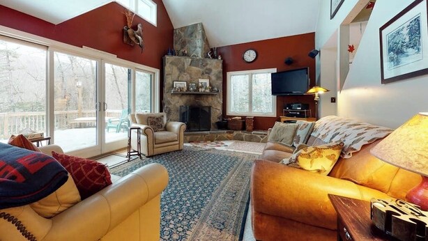Una sala de estar con chimenea de piedra, sofás de cuero, televisión y un ventanal con vista a una terraza.