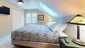 Un dormitorio con cama, ventilador de techo, lámpara, televisor y tragaluz.