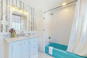 A bathroom with a white vanity, a blue bathtub, and a shower area with white tiles. - Cozy home with  covered porch, & sun room - walk to shops/dining/bars (Bethlehem)