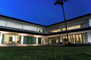 Una casa moderna de dos pisos con ventanas amplias, césped cuidado y una palmera.