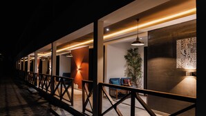 A modern hotel corridor with a wooden railing, a seating area with chairs, and a large potted plant.