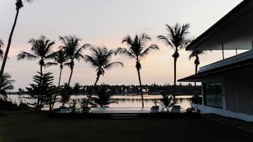 A modern building with a pool, surrounded by palm trees and a body of water.