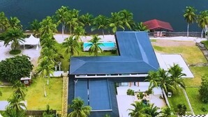 An aerial view of a coastal property with a swimming pool, palm trees, and a boat on the water.